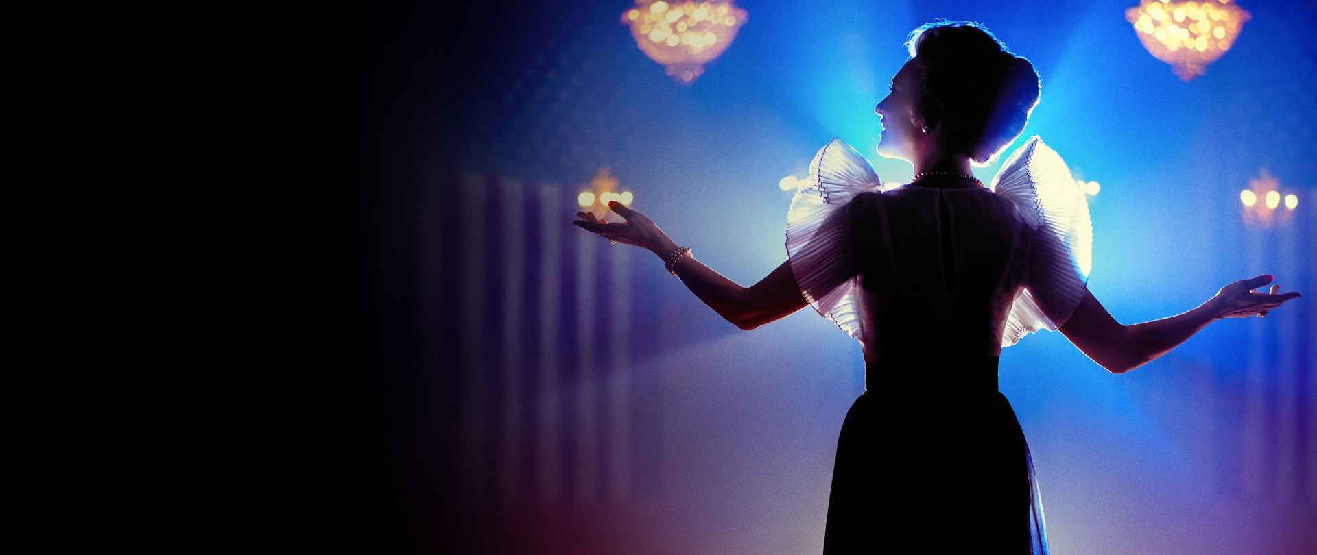 Spotlight shadowed silhouette of Cate Blanchett holding her arms out in a banquet hall with American flags in the background