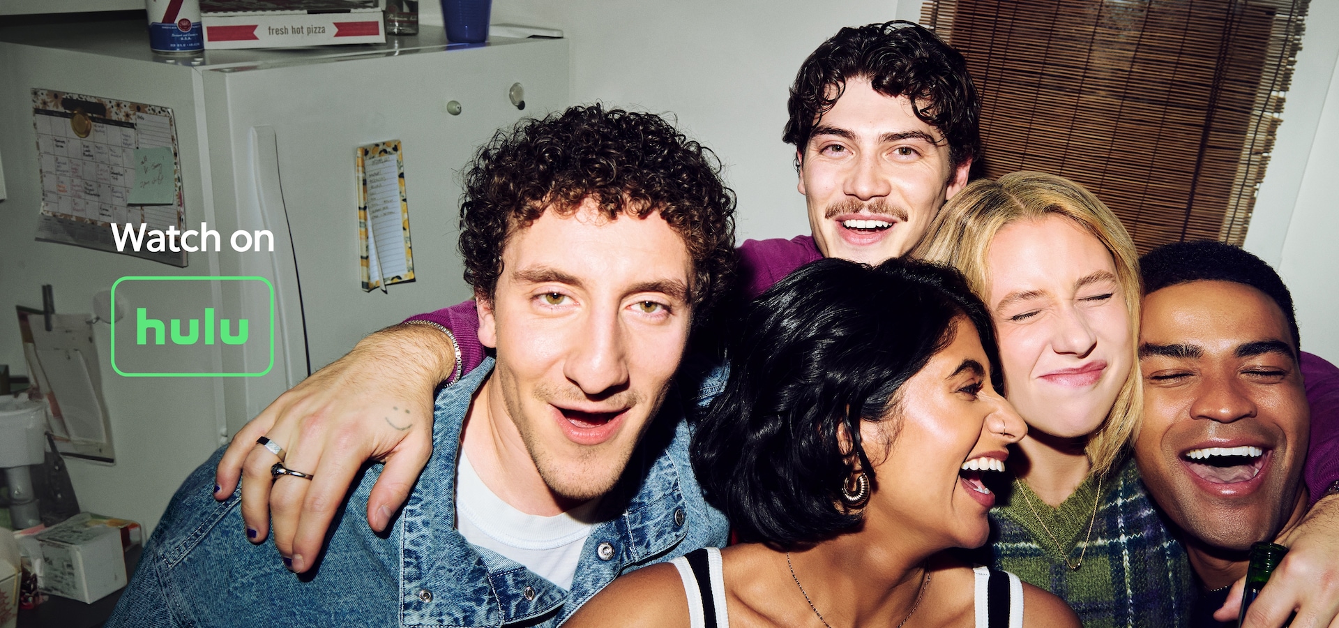 A group of five friends posing for a selfie while laughing in a small apartment kitchen.