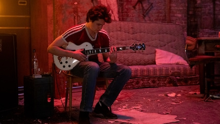 Man sitting on a chair playing a guitar in a room with pink lighting
